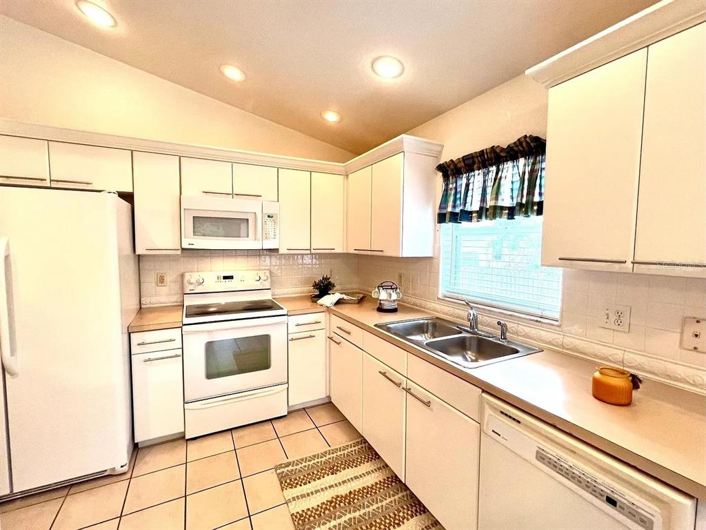 A kitchen features white cabinets, white appliances, a double sink, and tiled flooring — 1485 DONEGAN ROAD, LARGO, FL