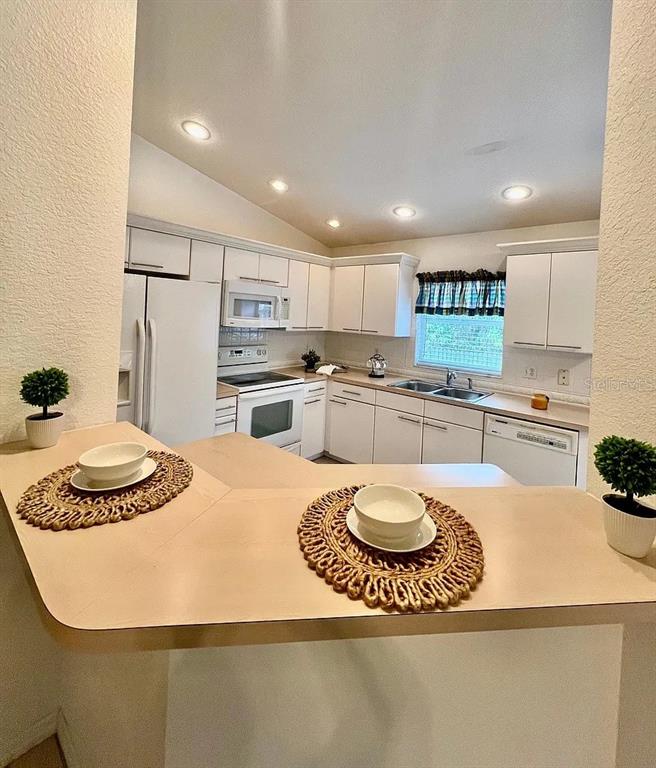A kitchen with white cabinets, light countertops, and a breakfast bar with two place settings — 1485 DONEGAN ROAD, LARGO, FL