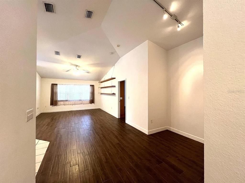 A living room with dark wood-look tile flooring, vaulted ceilings, and wall-mounted floating shelves — 1485 DONEGAN ROAD, LARGO, FL