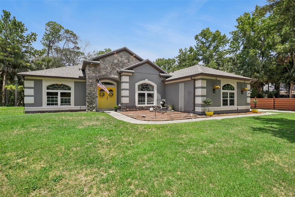 A single-story house with a stone facade, gray stucco walls, and a bright yellow front door — 5880 NOLAN ROAD, SANFORD, FL