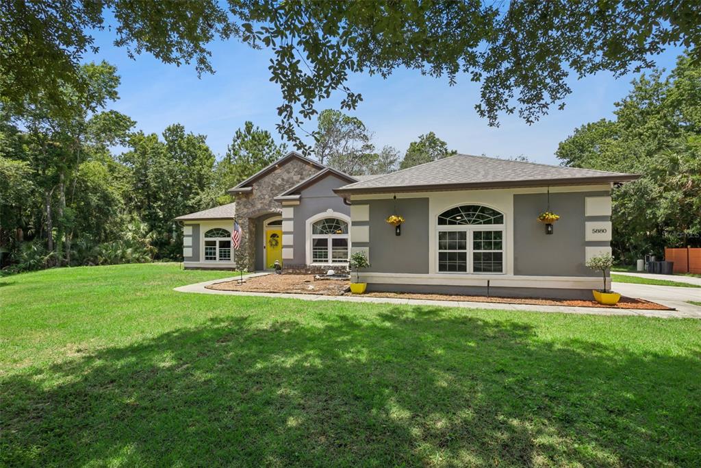 A single-story house with a gray stucco exterior, stone accents, and a bright yellow door — 5880 NOLAN ROAD, SANFORD, FL
