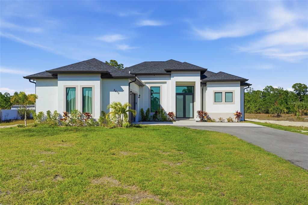 A modern, single-story white house with a dark roof and a paved driveway — 2415 56TH AVENUE NE, NAPLES, FL