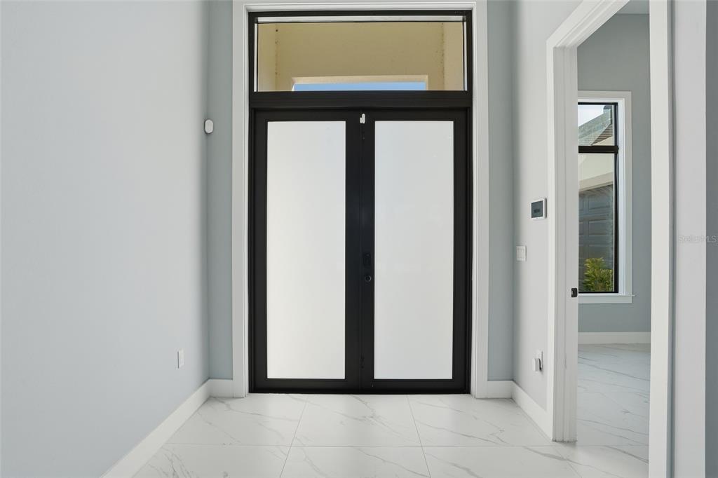 A modern entryway features double glass doors, white marble-look tile flooring, and light blue walls — 2415 56TH AVENUE NE, NAPLES, FL