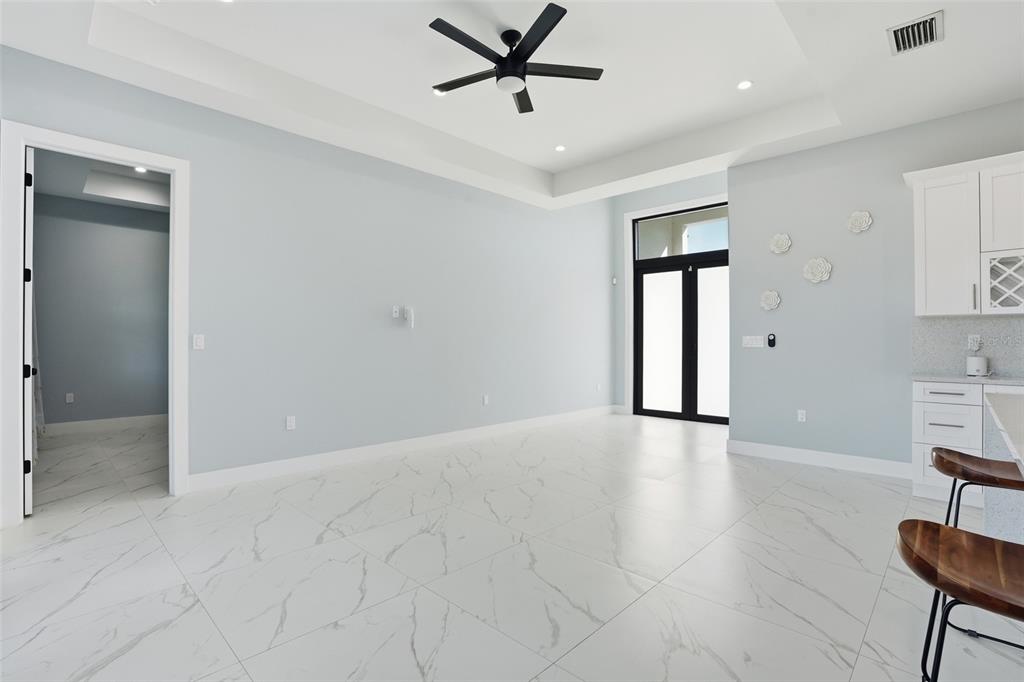 A bright room features white marble-look tile flooring, a tray ceiling, and a kitchen area — 2415 56TH AVENUE NE, NAPLES, FL