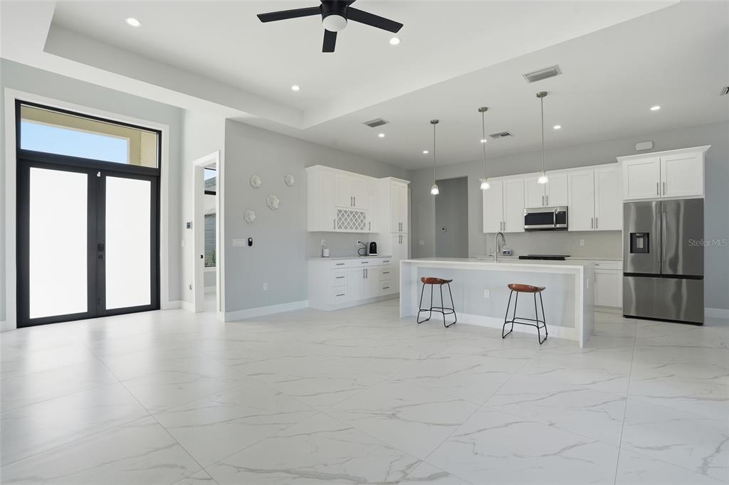 A modern open-concept kitchen and living area features white cabinetry, marble-look tile floors, and island seating — 2415 56TH AVENUE NE, NAPLES, FL