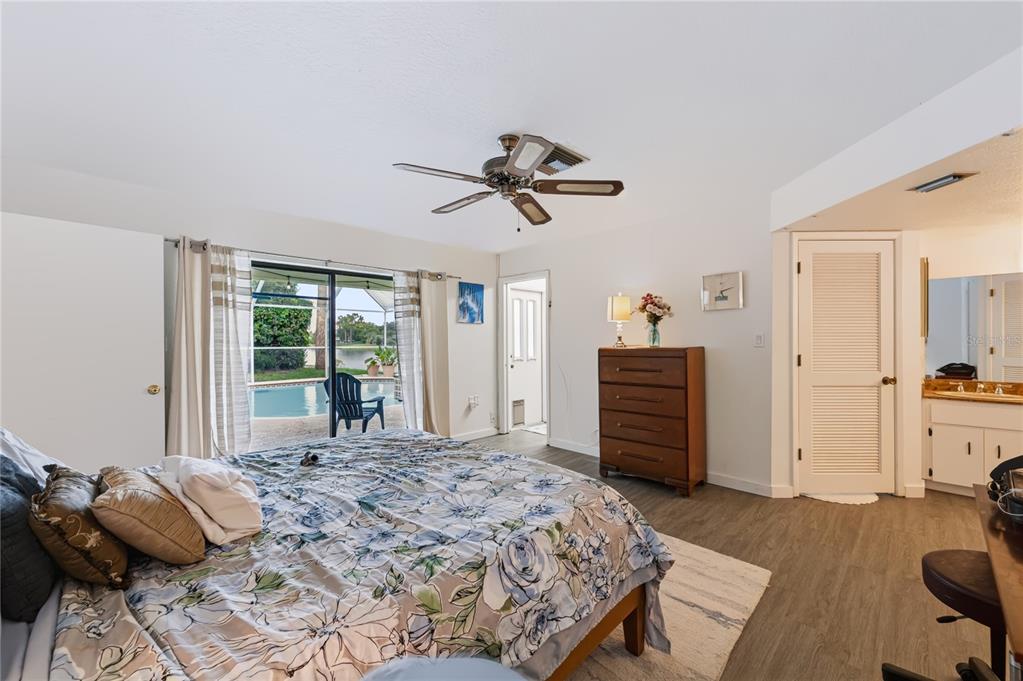 A bedroom with a floral bedspread, ceiling fan, dresser, and sliding doors opening to a pool — 9520 LAKE CHRISTINA LANE, PORT RICHEY, FL