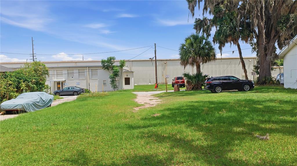 A grassy lot with a covered car, a parked SUV, and a large warehouse building behind — 1 CENTRAL WAREHOUSE, OCALA, FL