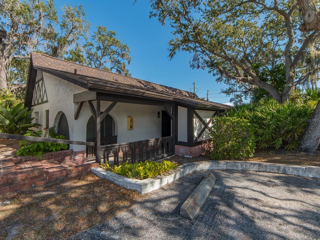 A Tudor-style building with a covered porch, brick steps, and a gravel parking area — 310 N BAYSHORE BOULEVARD UNIT 103, CLEARWATER, FL