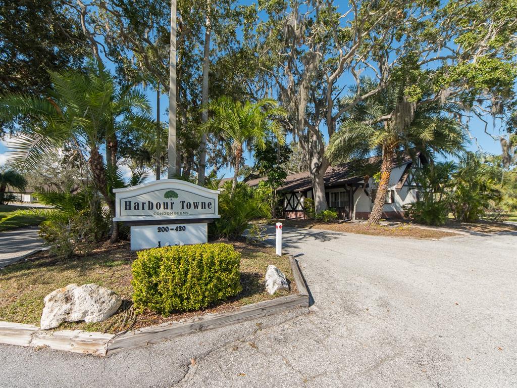 A sign for Harbour Towne Condominiums stands near a paved driveway and mature trees — 310 N BAYSHORE BOULEVARD UNIT 103, CLEARWATER, FL