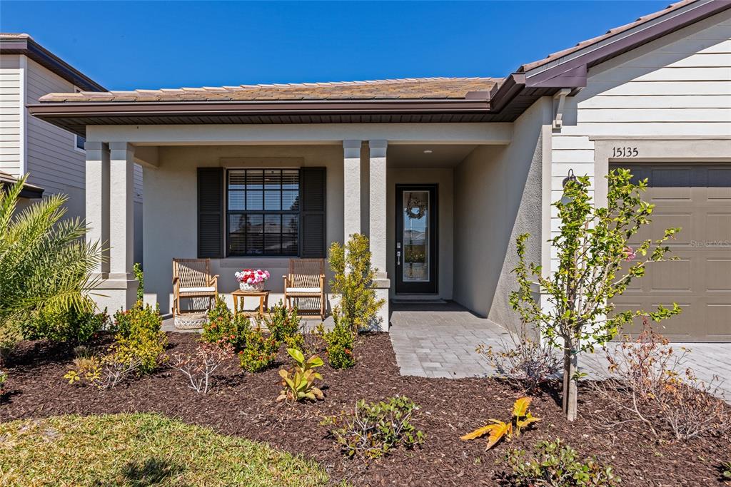 The exterior of a single-story house features a covered porch, a front door, and landscaping — 15135 OXFORD GREY DRIVE, BRADENTON, FL