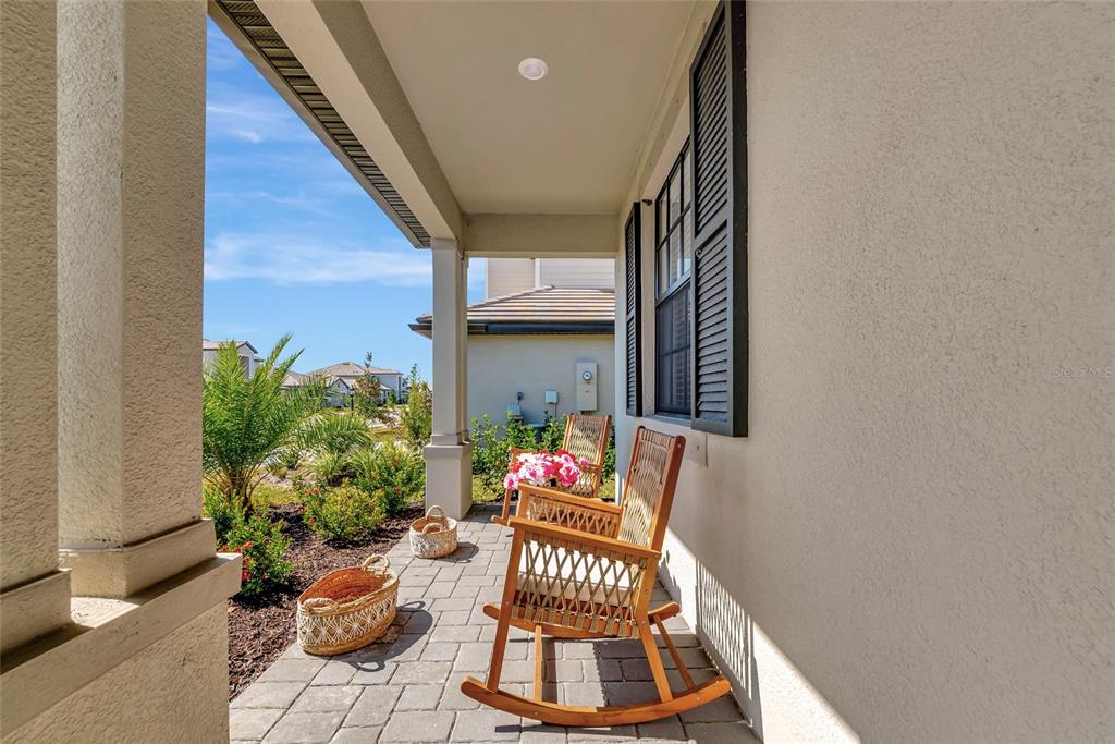 A covered front porch features stone pavers, two wooden rocking chairs, and a small basket — 15135 OXFORD GREY DRIVE, BRADENTON, FL