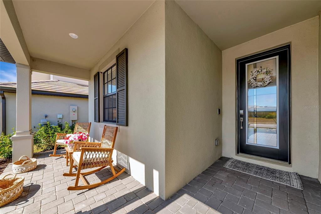 A covered front porch features a brick paver floor, two rocking chairs, and a glass-paneled door — 15135 OXFORD GREY DRIVE, BRADENTON, FL
