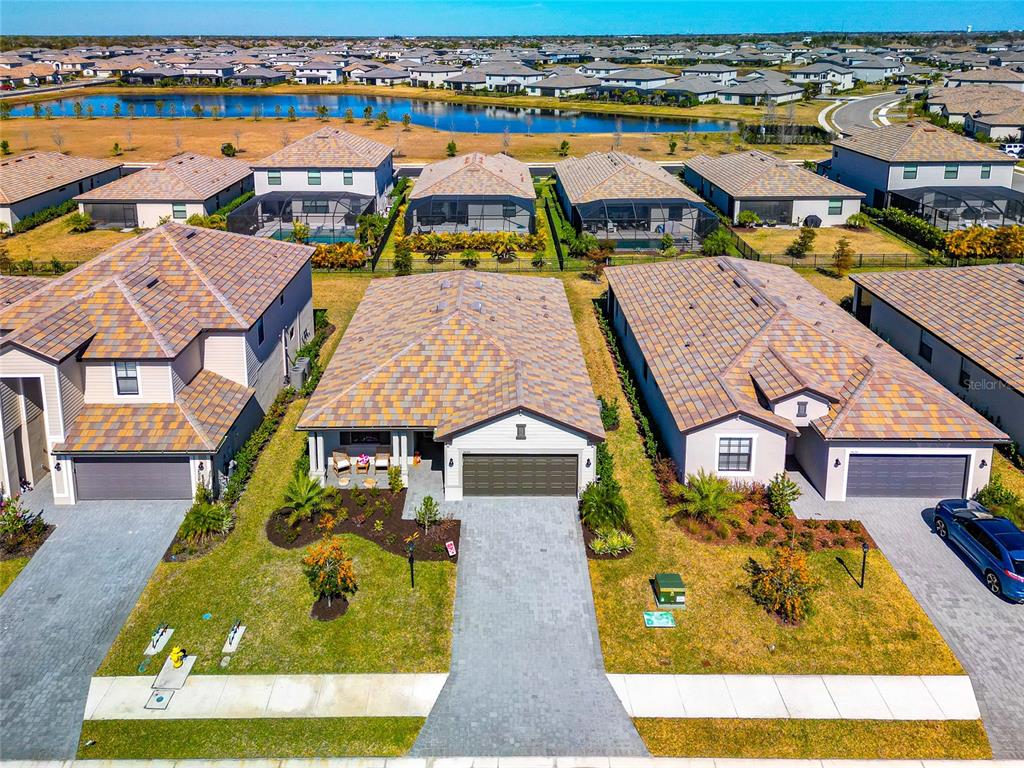 An aerial view shows three suburban houses with tiled roofs and paved driveways near a lake — 15135 OXFORD GREY DRIVE, BRADENTON, FL