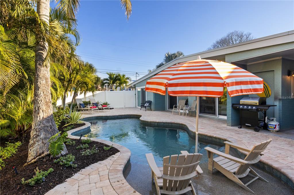 A backyard features a swimming pool, patio furniture, a striped umbrella, and a gas grill — 312 HARDIN AVENUE, ANNA MARIA, FL