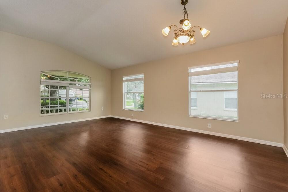 An empty room with dark wood flooring, beige walls, and a decorative chandelier — 812 LESA GLEN PLACE, BRANDON, FL