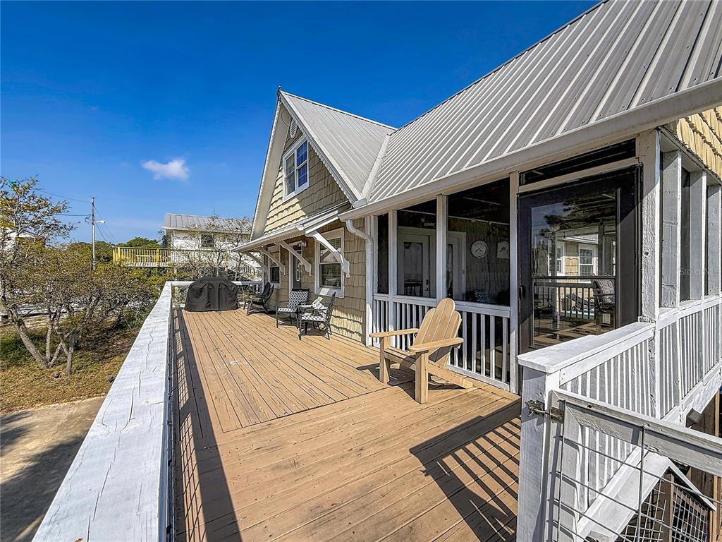 A wooden deck features a screened-in porch, outdoor seating, and a metal roof — 7 BASS STREET, PANACEA, FL
