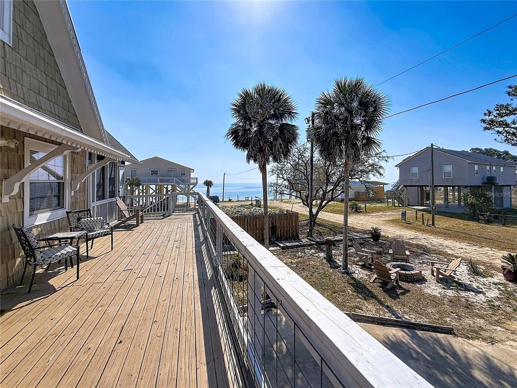 A wooden deck overlooks a sandy yard with palm trees and a view of the ocean — 7 BASS STREET, PANACEA, FL