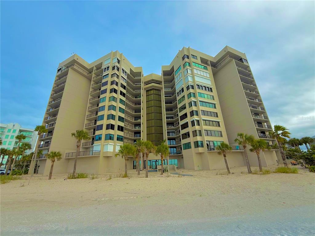 A multi-story tan condominium building stands on a sandy beach under a cloudy sky — 1600 GULF BOULEVARD UNIT 1112, CLEARWATER BEACH, FL