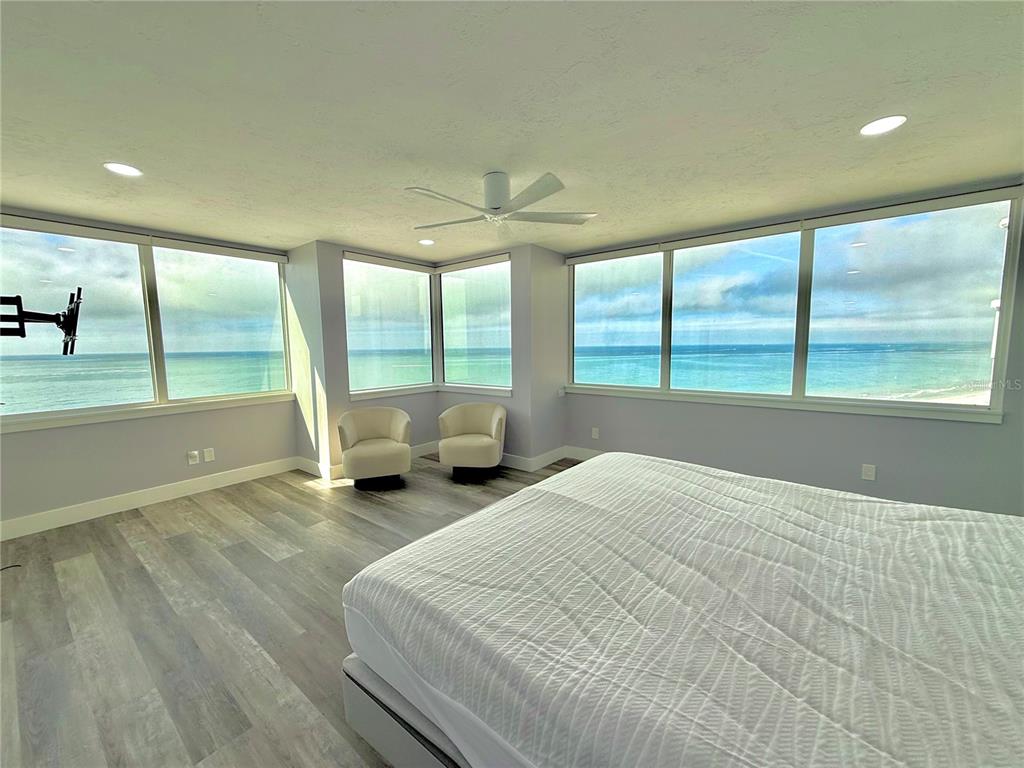 A bedroom with light wood-look flooring, a large bed, and floor-to-ceiling windows overlooking the ocean — 1600 GULF BOULEVARD UNIT 1112, CLEARWATER BEACH, FL