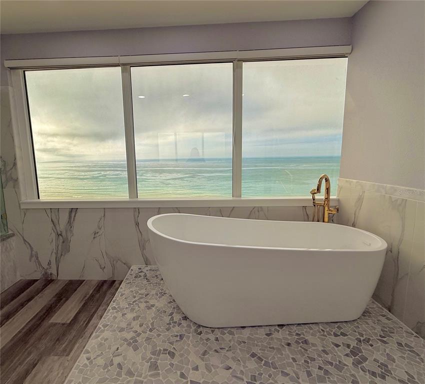A white freestanding bathtub sits on a mosaic tile platform before a large ocean-view window — 1600 GULF BOULEVARD UNIT 1112, CLEARWATER BEACH, FL