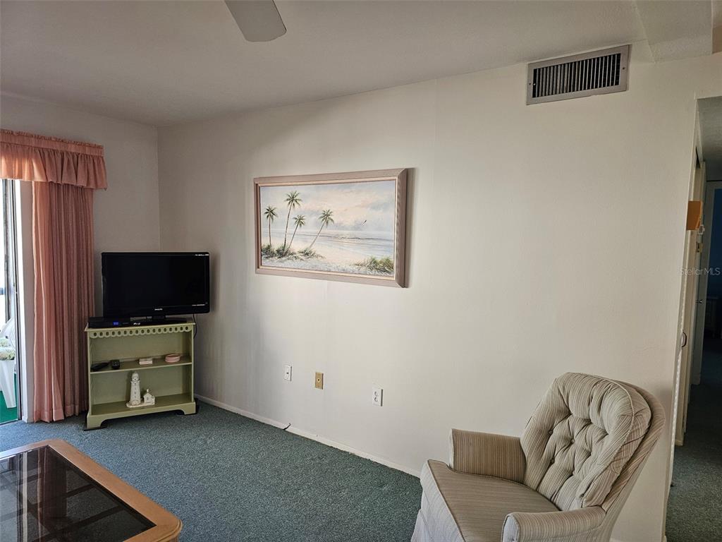 A living room features a wooden hutch, a blue sofa, a green armchair, and a balcony — 5906 GARDEN LANE UNIT A22, BRADENTON, FL