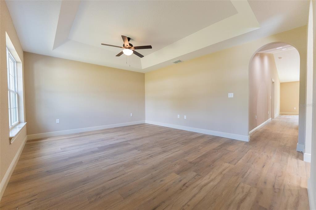 An empty room with light wood flooring, a tray ceiling, and an arched entryway — 7722 SW 146TH LANE ROAD, OCALA, FL