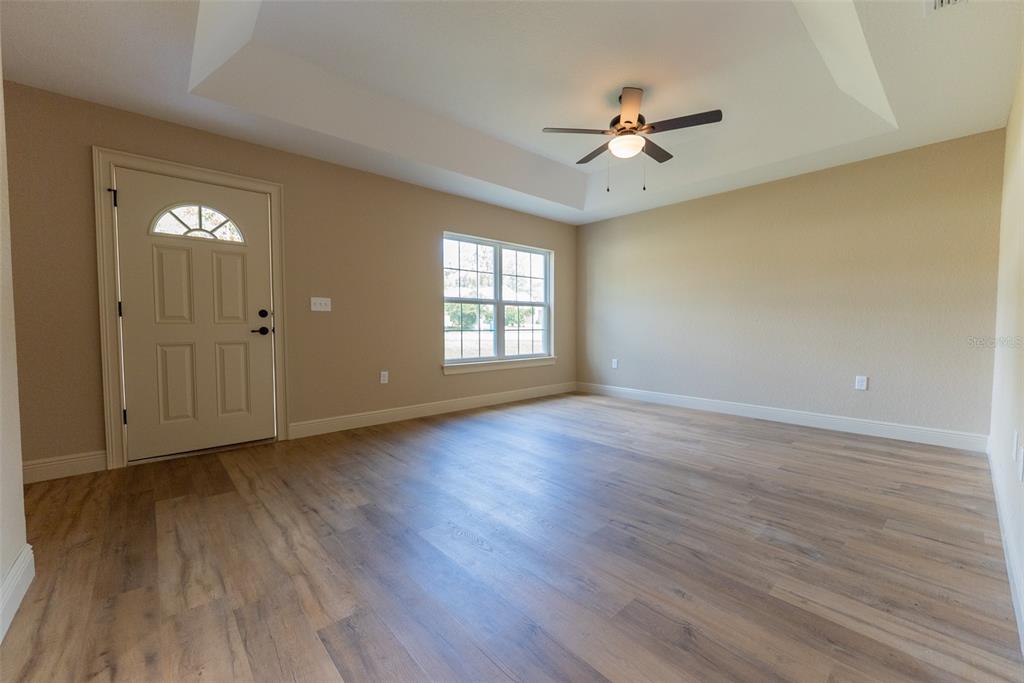 An empty room with light wood-look flooring, a tray ceiling, and a single exterior door — 7722 SW 146TH LANE ROAD, OCALA, FL