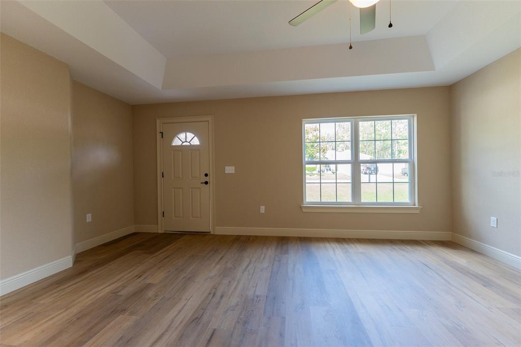 An empty room with light wood-look flooring, beige walls, a ceiling fan, and a door — 7722 SW 146TH LANE ROAD, OCALA, FL