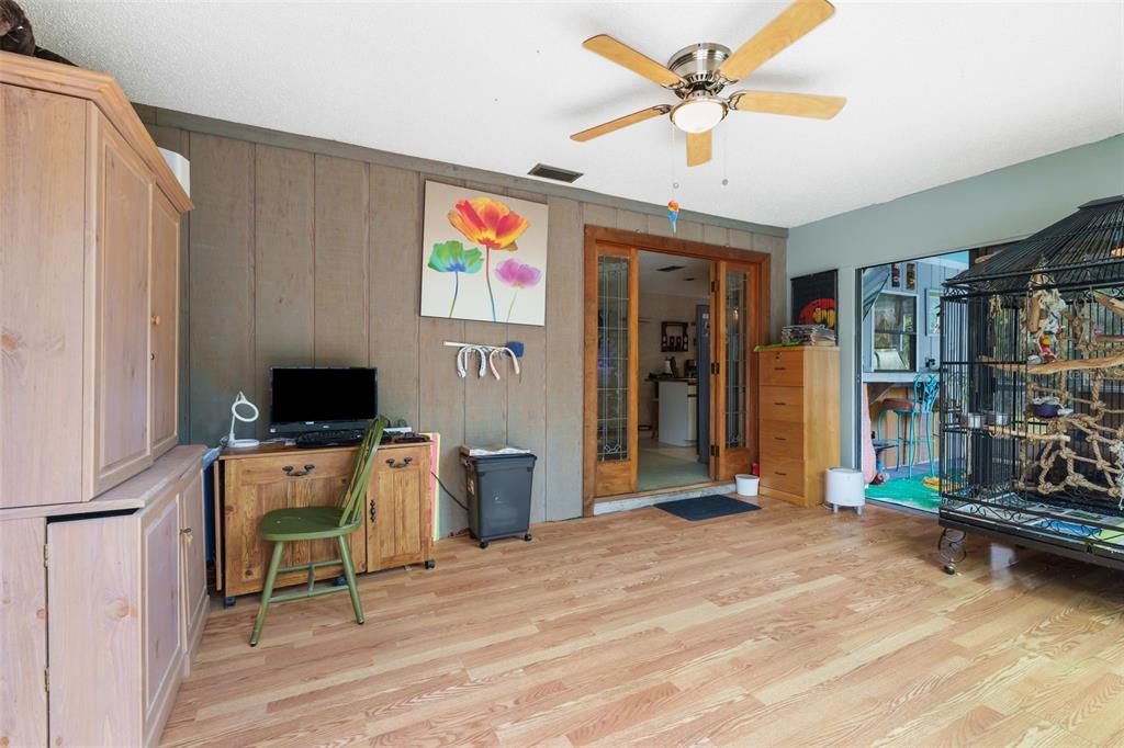 A room with wood-paneled walls, a ceiling fan, a computer desk, and a large birdcage — 2070 59TH STREET, SARASOTA, FL