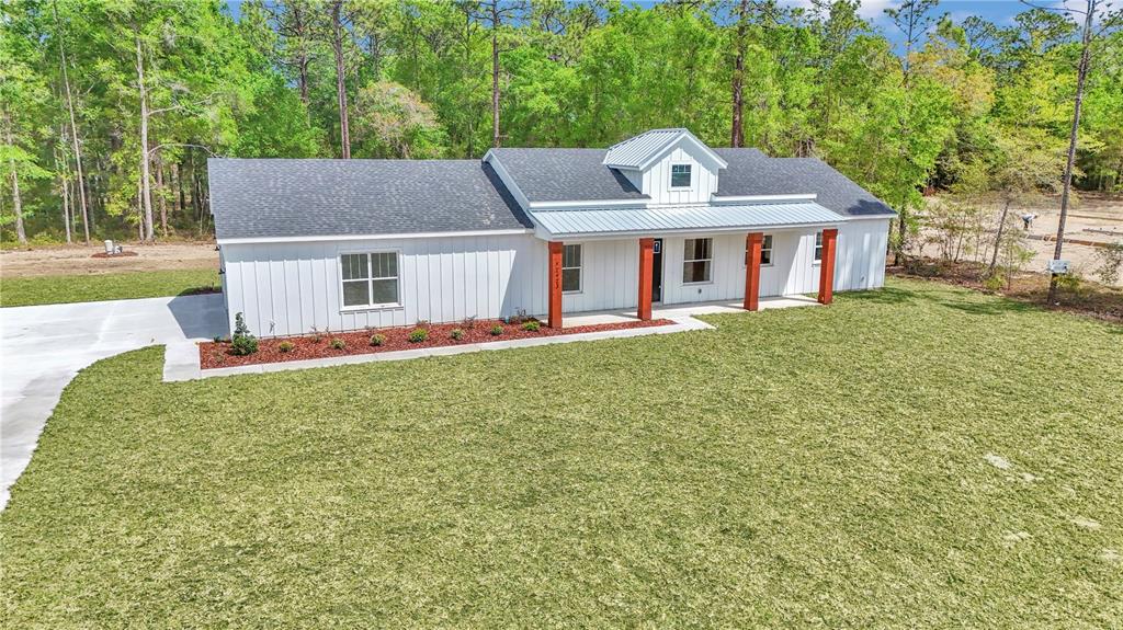 A white farmhouse with a metal porch roof and wood columns sits on a grassy lot — 12423 SW 45 STREET, OCALA, FL