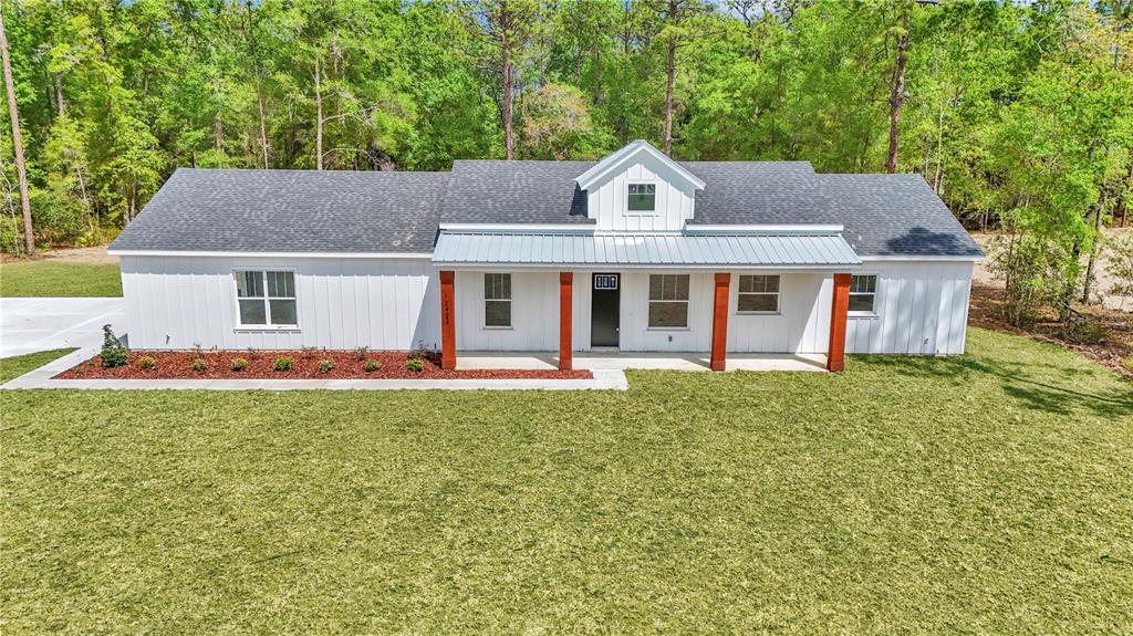 A white farmhouse-style home with a metal roof and wooden porch posts sits on grass — 12423 SW 45 STREET, OCALA, FL