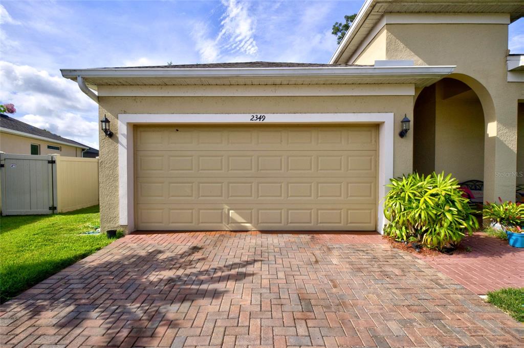 A beige garage door with a brick driveway and a small patch of green lawn — 2349 JERNIGAN LOOP, KISSIMMEE, FL
