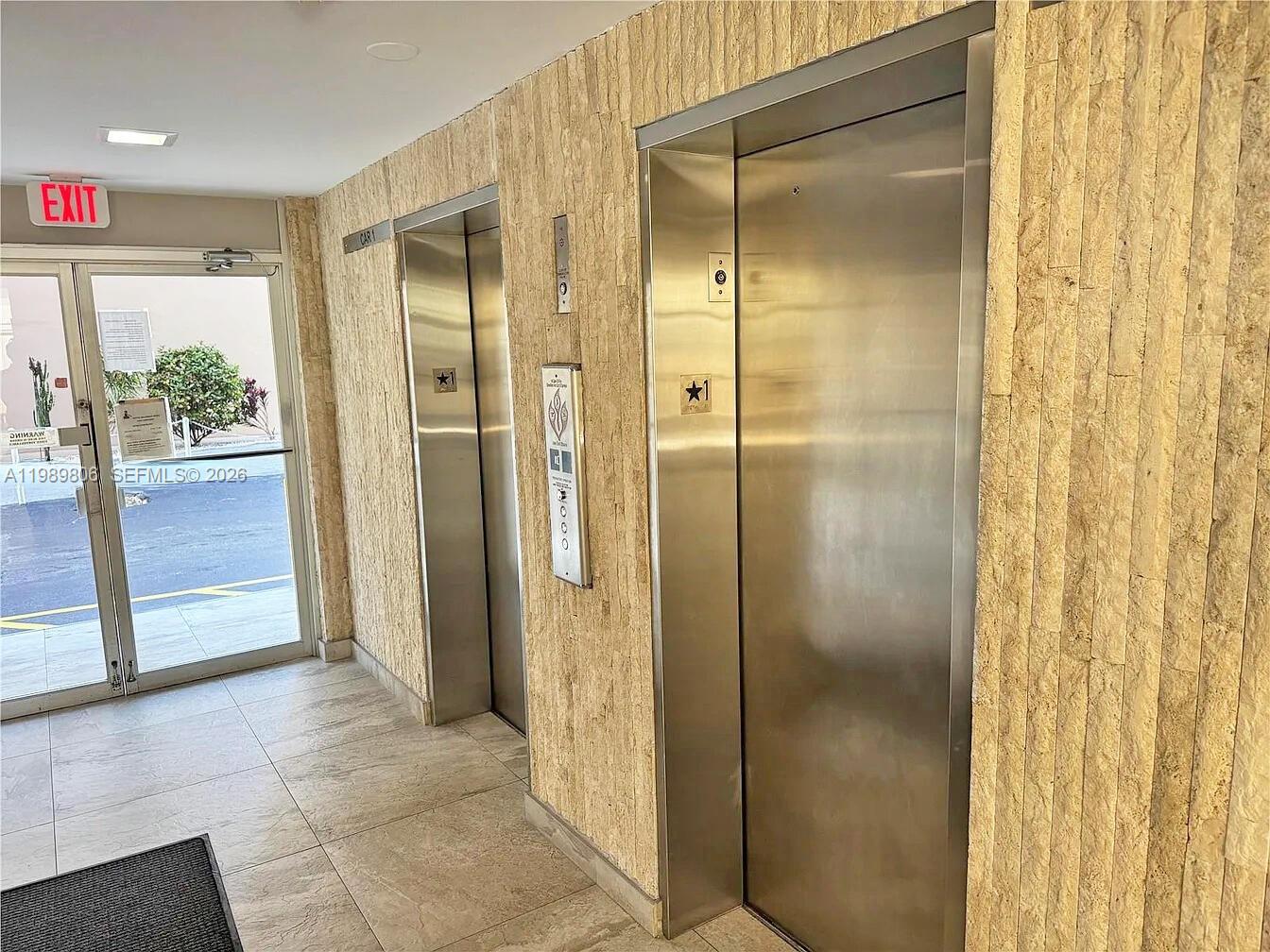 Two stainless steel elevators are set into a textured stone wall beside a glass door — 3113 S Ocean Dr # 504, Hallandale Beach FL 33009, HALLANDALE BEACH, FL