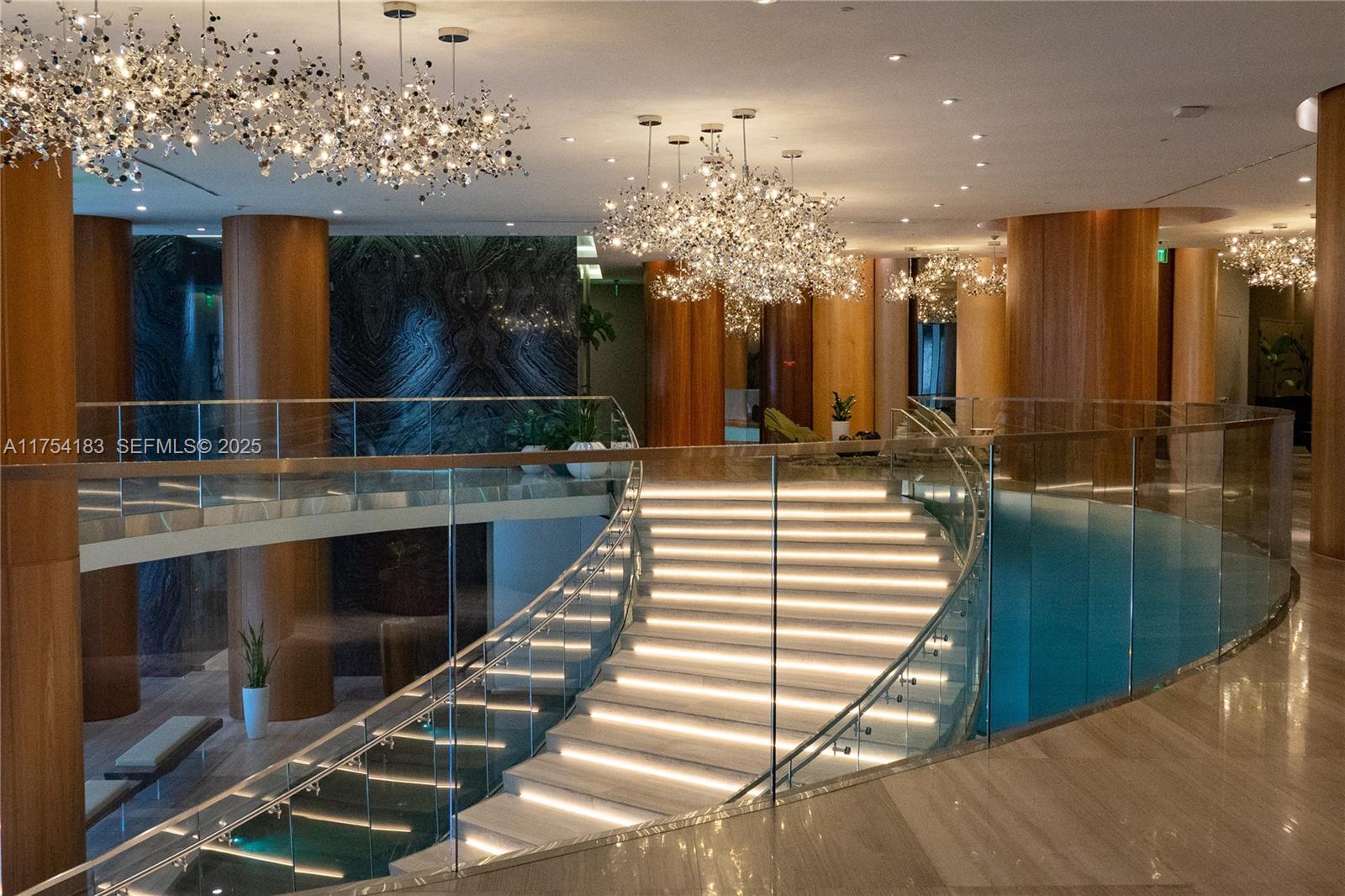 A grand staircase with illuminated steps and glass railings sits in a modern lobby — 488 NE 18 St # 1809, Miami FL 33132, MIAMI, FL
