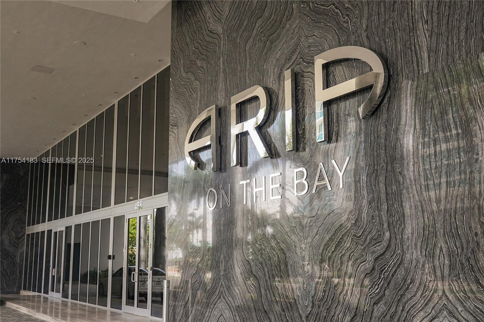 The building entrance features a polished stone wall with large metallic signage and glass doors — 488 NE 18 St # 1809, Miami FL 33132, MIAMI, FL