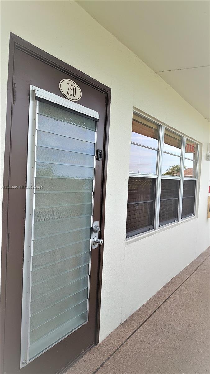 A brown door with a louvered glass insert and a window are on a building exterior — 250 Suffolk F # 250, Boca Raton FL 33434, BOCA RATON, FL