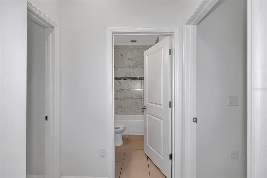 A hallway leads to a bathroom featuring a tiled tub surround and a white door — 3650 SW 128TH PLACE, OCALA, FL