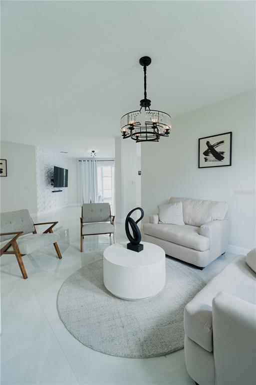 A bright living room features white tile floors, a round rug, and a modern chandelier — 1014 CORVINA DRIVE, DAVENPORT, FL