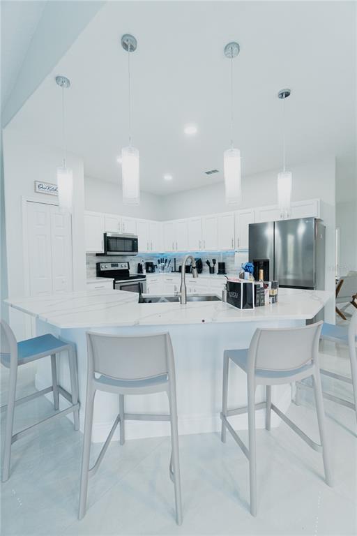 A modern kitchen features white cabinetry, a marble-topped island, and four gray bar stools — 1014 CORVINA DRIVE, DAVENPORT, FL