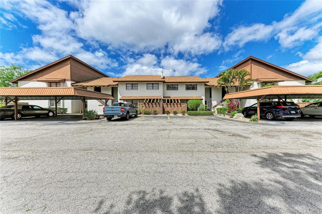 A two-story apartment building with covered parking spaces in front under a blue sky — 4578 RED MAPLE ROAD UNIT 904, BRADENTON, FL