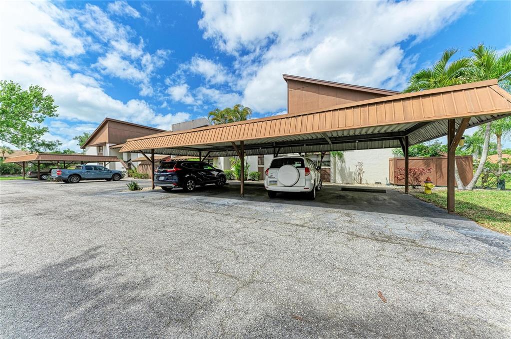 A parking area features a long metal carport structure shading several parked vehicles — 4578 RED MAPLE ROAD UNIT 904, BRADENTON, FL
