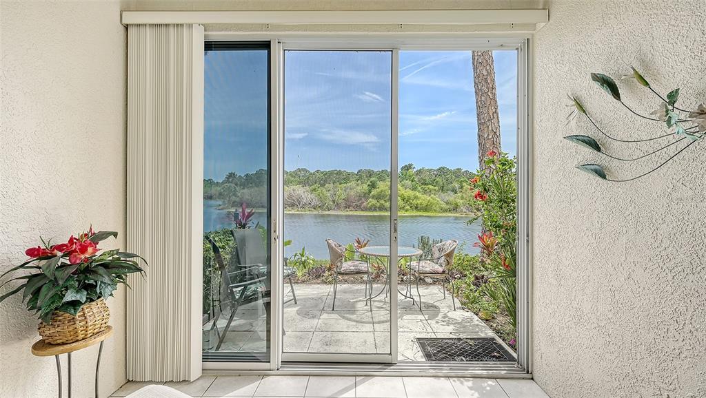 A sliding glass door opens to a patio overlooking a lake with outdoor furniture — 8350 WINGATE DRIVE UNIT 913, SARASOTA, FL