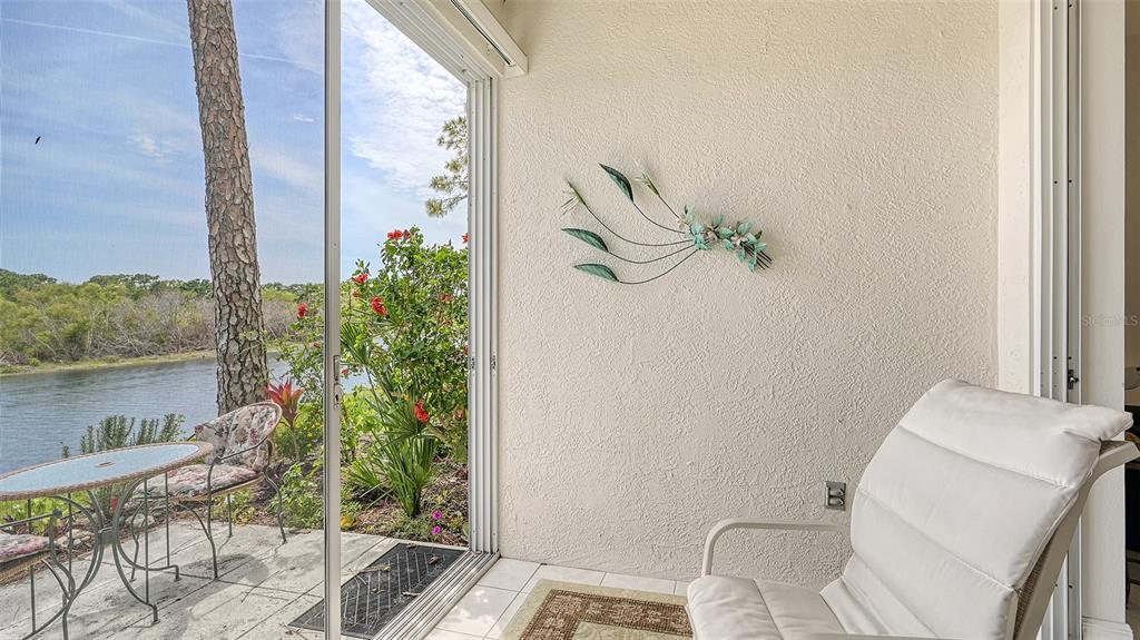 A sunroom features a white chair, a small patio table, and sliding doors overlooking a river — 8350 WINGATE DRIVE UNIT 913, SARASOTA, FL