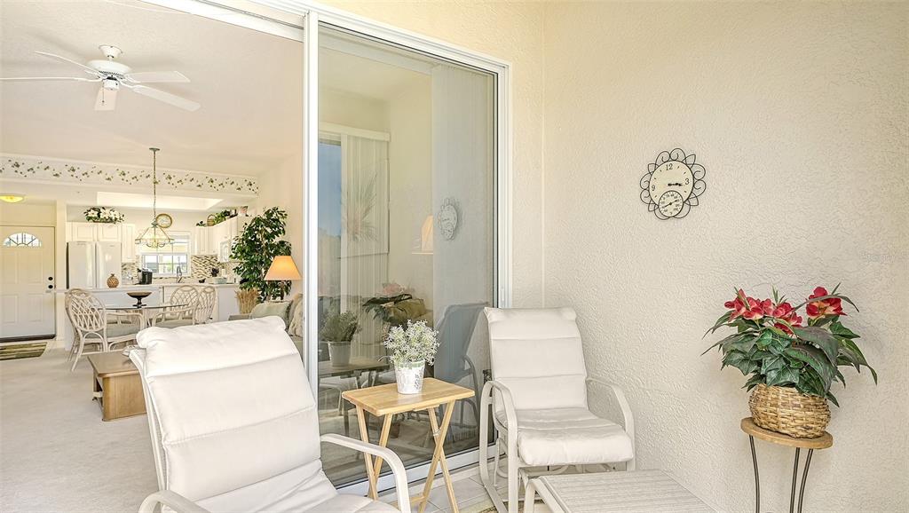 A covered patio with two white chairs and a small table overlooks an interior living space — 8350 WINGATE DRIVE UNIT 913, SARASOTA, FL