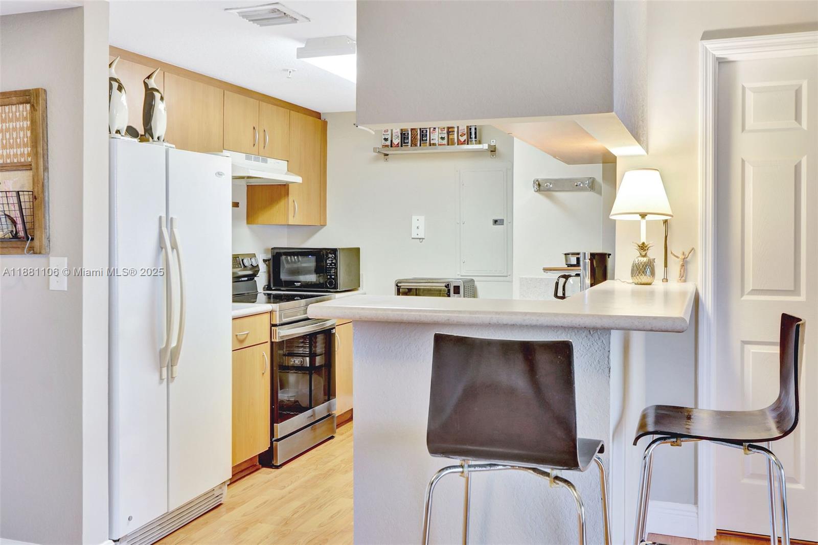 A kitchen features light wood cabinets, stainless steel appliances, and a breakfast bar with stools — 816 NW 11th St # 905, Miami FL 33136, MIAMI, FL