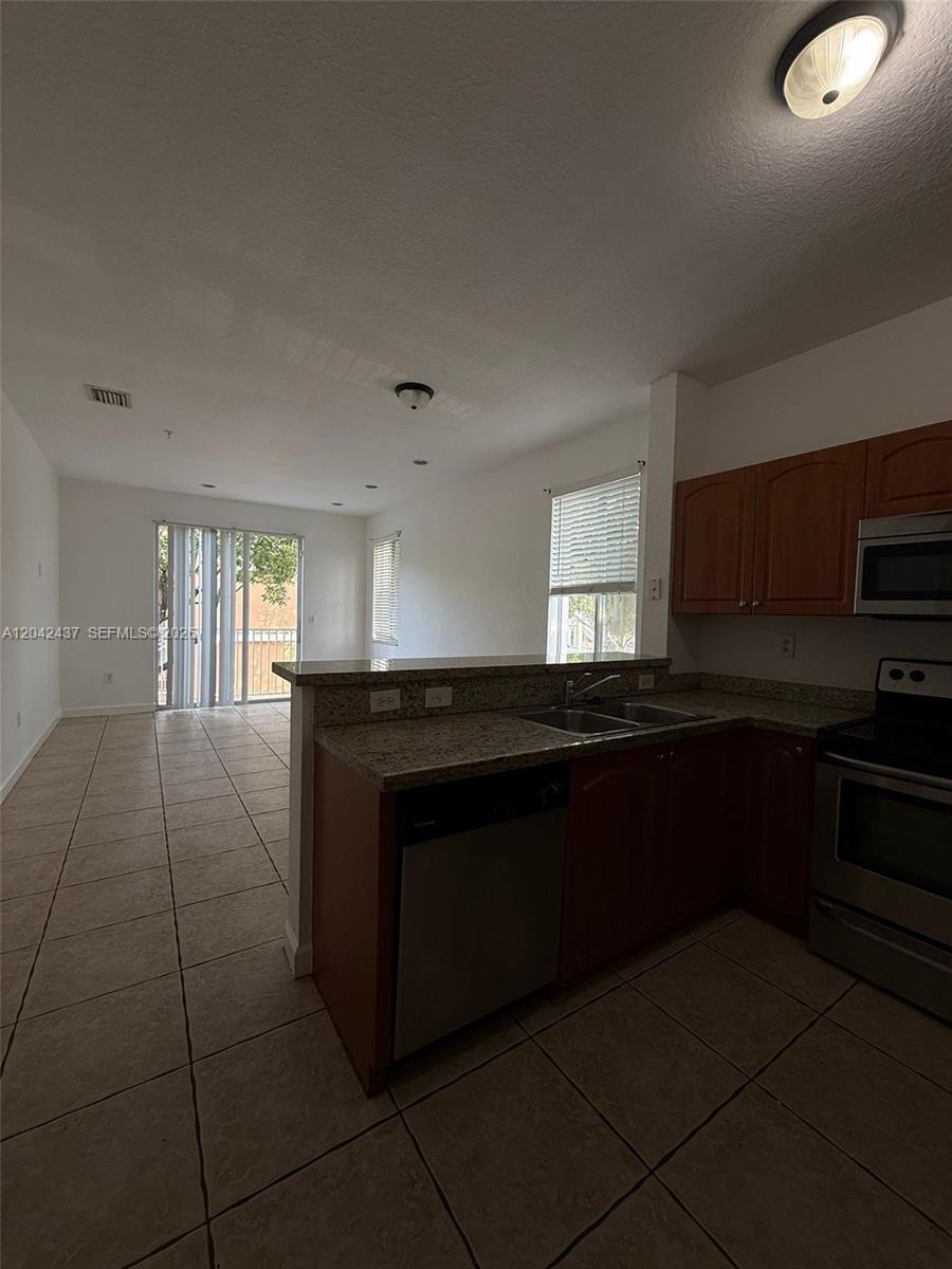 A kitchen with granite countertops and stainless steel appliances opens to a tiled living area — 17640 NW 73rd Ave # 19, Hialeah FL 33015, HIALEAH, FL