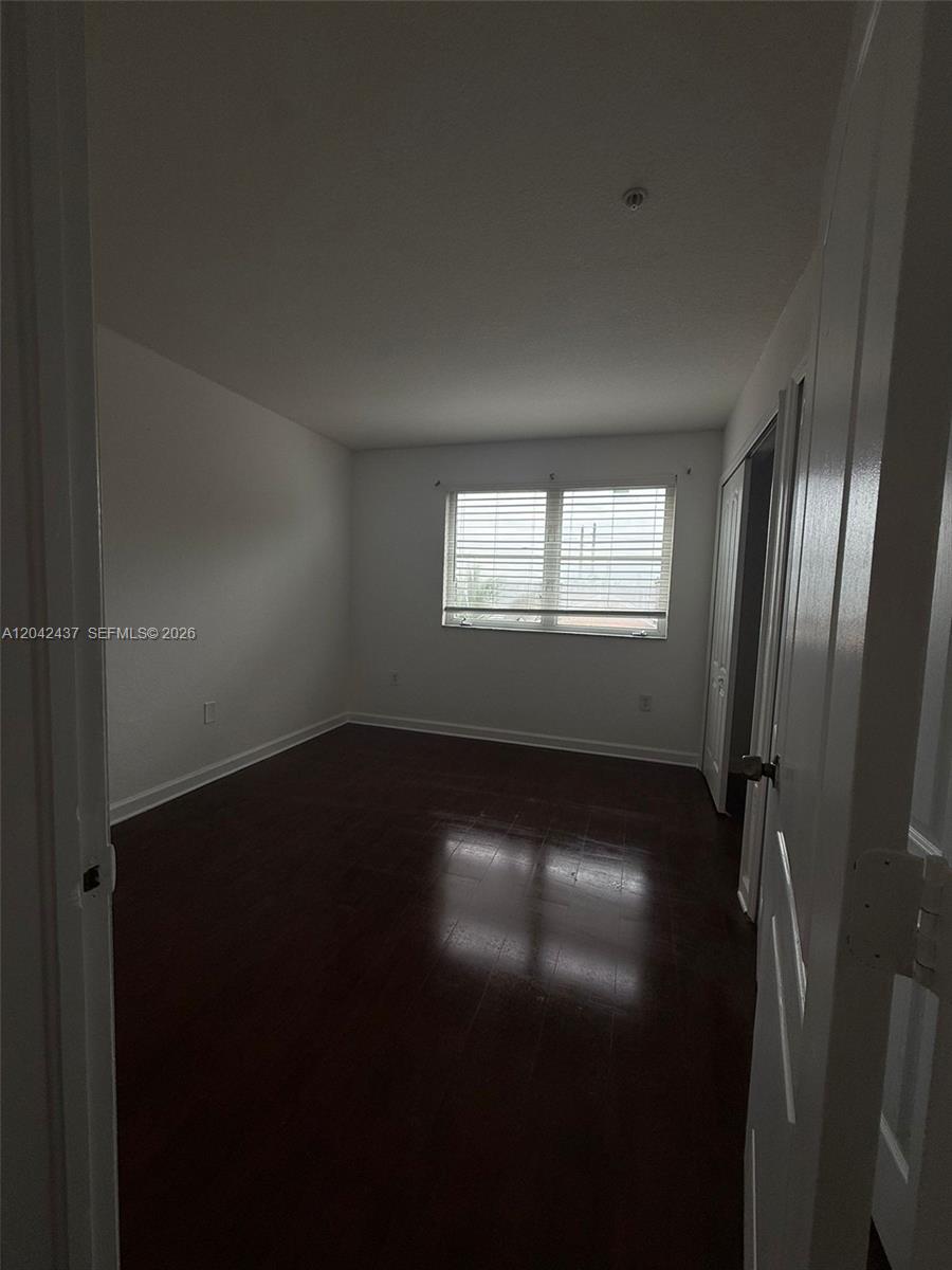 An empty bedroom features dark wood flooring, white walls, and a window with blinds — 17640 NW 73rd Ave # 19, Hialeah FL 33015, HIALEAH, FL