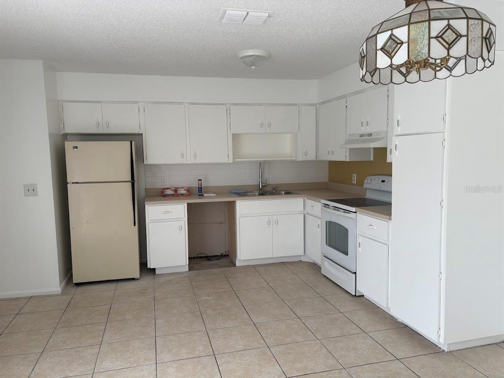 A kitchen features white cabinets, a beige refrigerator, a white stove, and light-colored floor tiles — 7467 MEAD DRIVE, SPRING HILL, FL