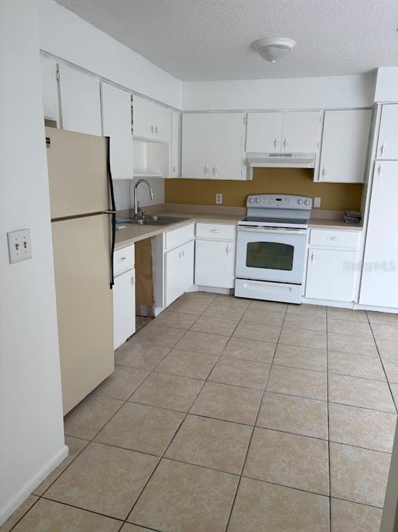 A kitchen features white cabinets, a beige refrigerator, a white stove, and tan tile flooring — 7467 MEAD DRIVE, SPRING HILL, FL