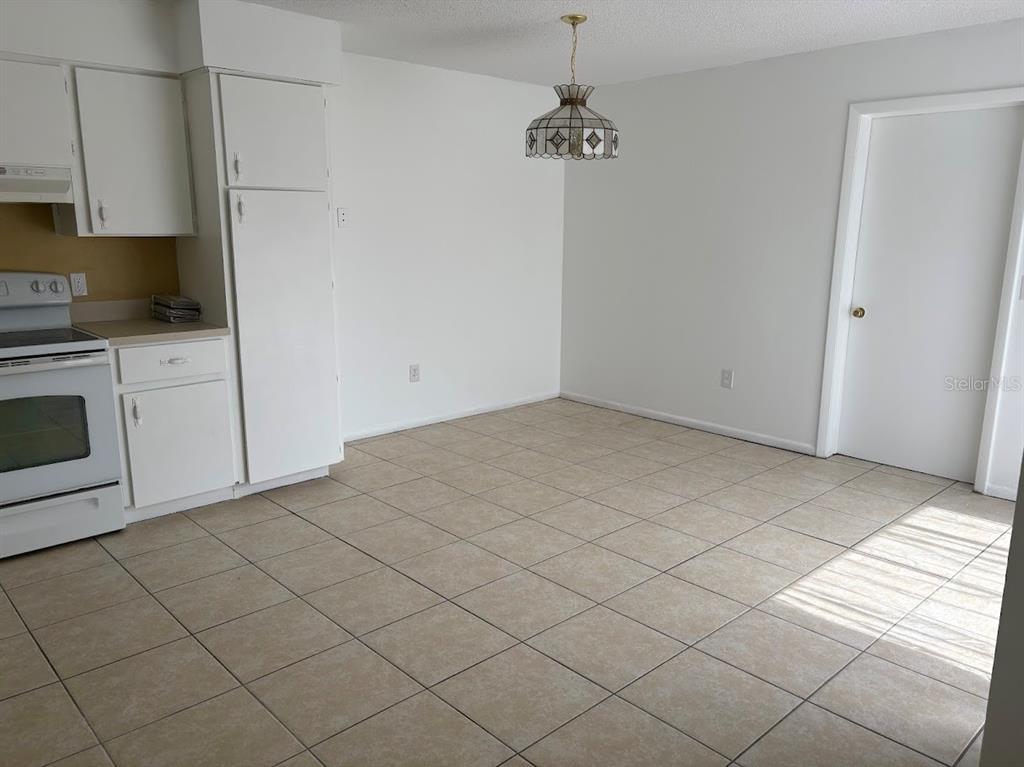 A kitchen and dining area with white cabinets, a white stove, and tiled flooring — 7467 MEAD DRIVE, SPRING HILL, FL